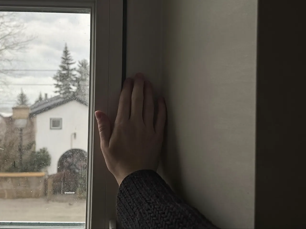 A hand held to the edge of a closed window to feel for a cold draught