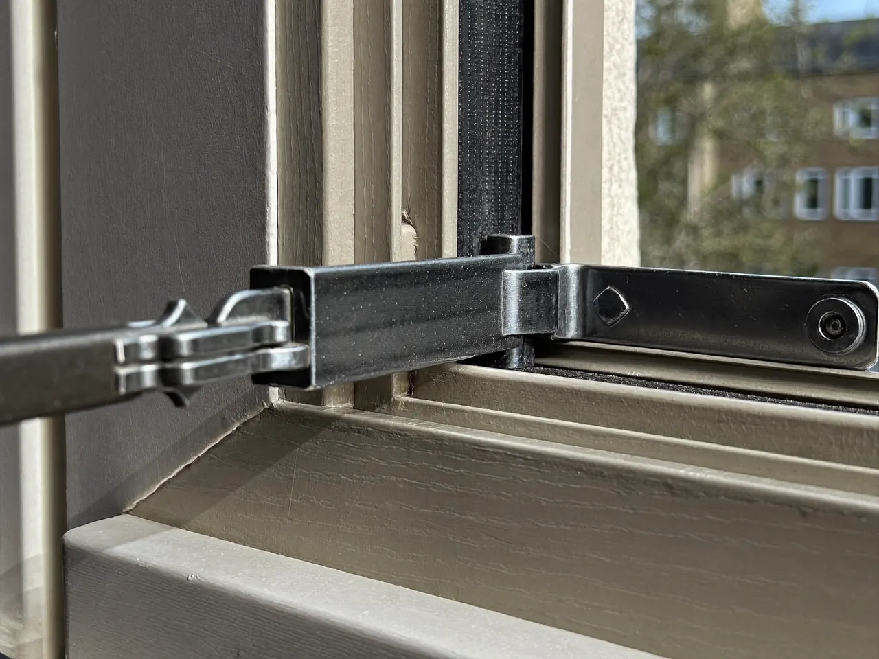 Close-up of a friction hinge and locking mechanism along the edge of a window sash
